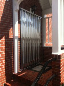 Accordion hurricane gate securing a red brick home entryway.