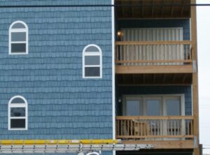 Blue shingle coastal home with wooden balconies and construction scaffolding.