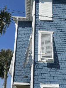 Blue shingle beach house with white hurricane shutters.