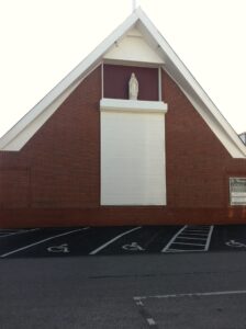 Red brick church: white statue protected by storm panels.