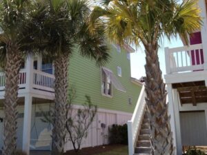 Green beach house with palms, raised for hurricane resilience.