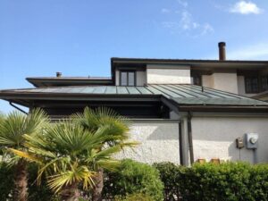 Sunlit modern coastal home in Wilmington with a green patina roof, showcasing durable construction and lush landscaping, emphasizing hurricane protection features.