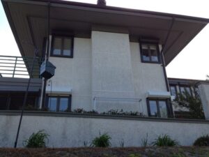 Modern stucco house, dark roof, hurricane shutters for privacy.