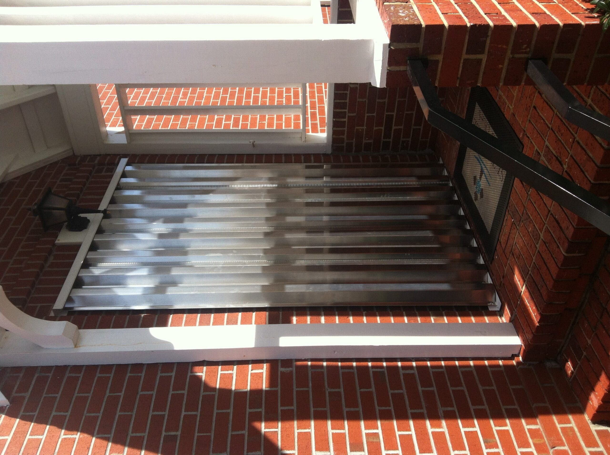 - american hurricane shutters Accordion hurricane gate securing a red brick home entryway.