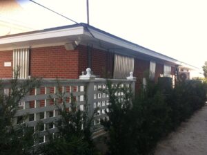 Secure red brick home with hurricane shutters and white privacy fence.