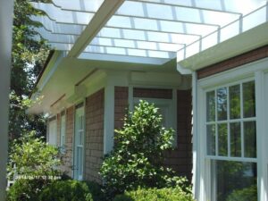 Elegant shingled home, modern white pergola, hurricane shutters.