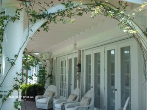 Elegant white porch with vine arch, French doors, wicker chairs.