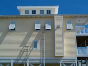Light yellow Topsail Island beach house with white accordion hurricane shutters.