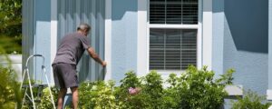 Man installs hurricane shutters on blue house, Wilmington.