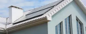 Modern periwinkle home with solar panels on white barrel tile roof.