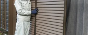 Coastal worker installs brown slatted hurricane shutters.