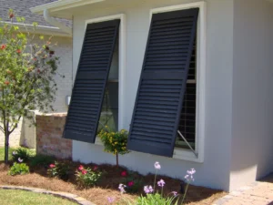 Dark louvered hurricane shutters, stucco home, vibrant garden.