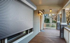 Grey home exterior: hurricane shutter, wooden porch, white railings.