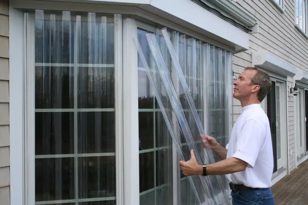 Man installing clear storm panels on a window for hurricane protection. Storm panel installation ensures home safety