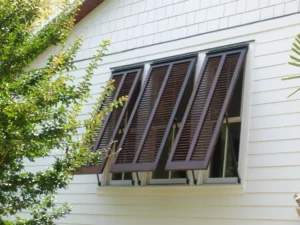 Dark brown louvered hurricane shutters open on white clapboard house.