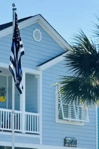 Mobile Image of a Thin Blue Line flag, blue coastal house, white shutters, palm tree, sunny.