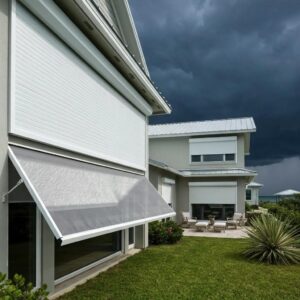 Modern coastal home with roll-down hurricane shutters partially closed against a stormy sky